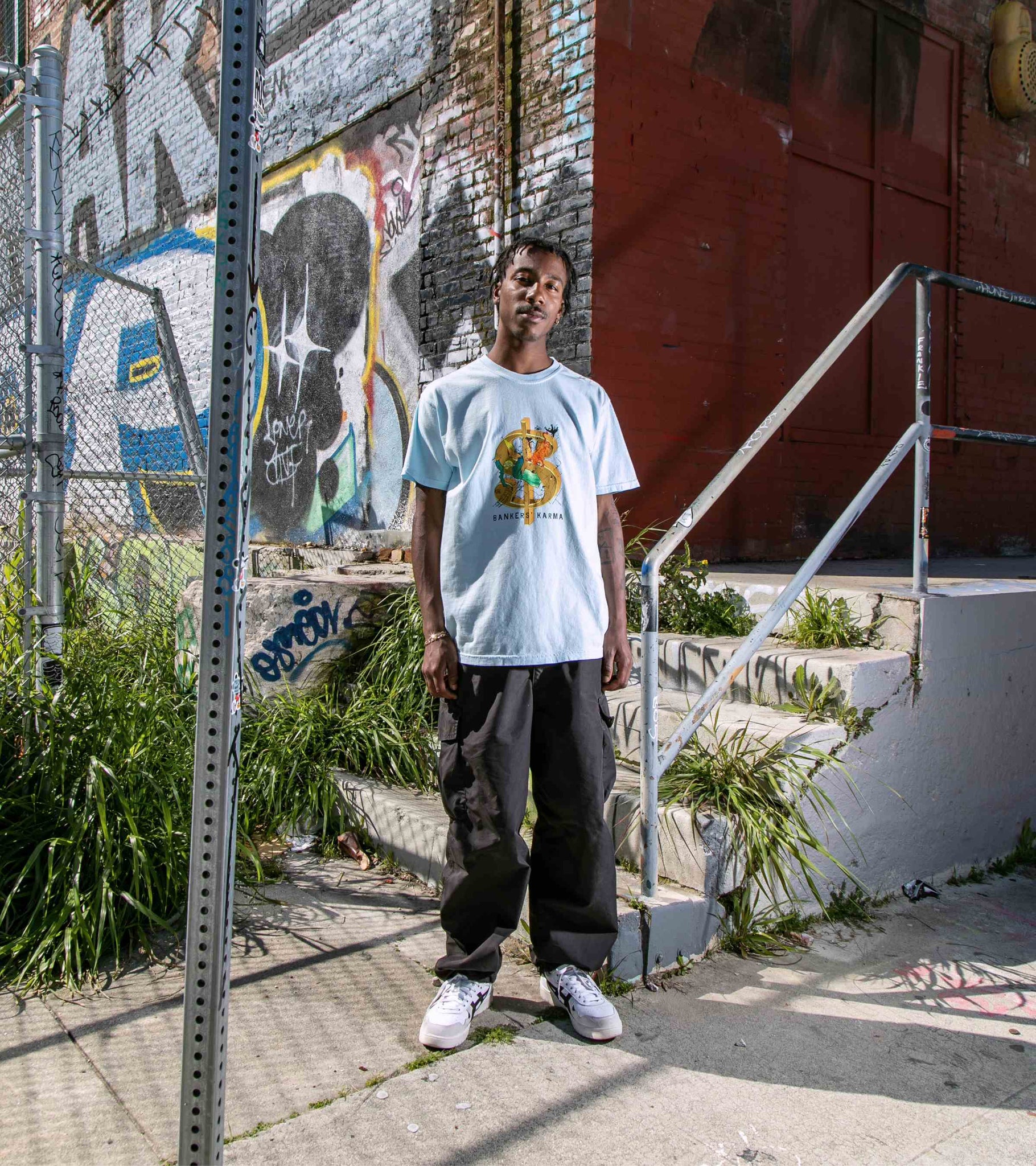 Wide shot of male model wearing unisex cotton graphic t-shirt in chambray blue with Bankers Karma graphic print visible.