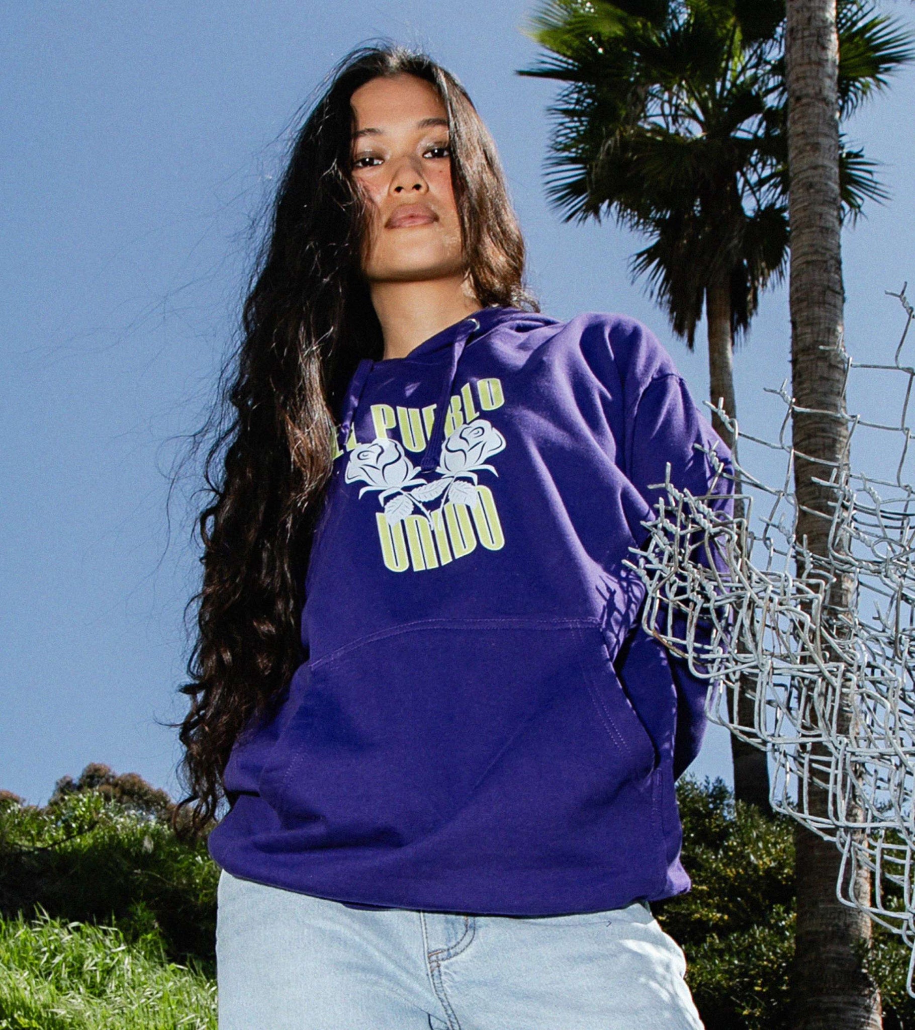 Medium shot of woman in purple classic fit midweight hoodie with El Pueblo Unido front print