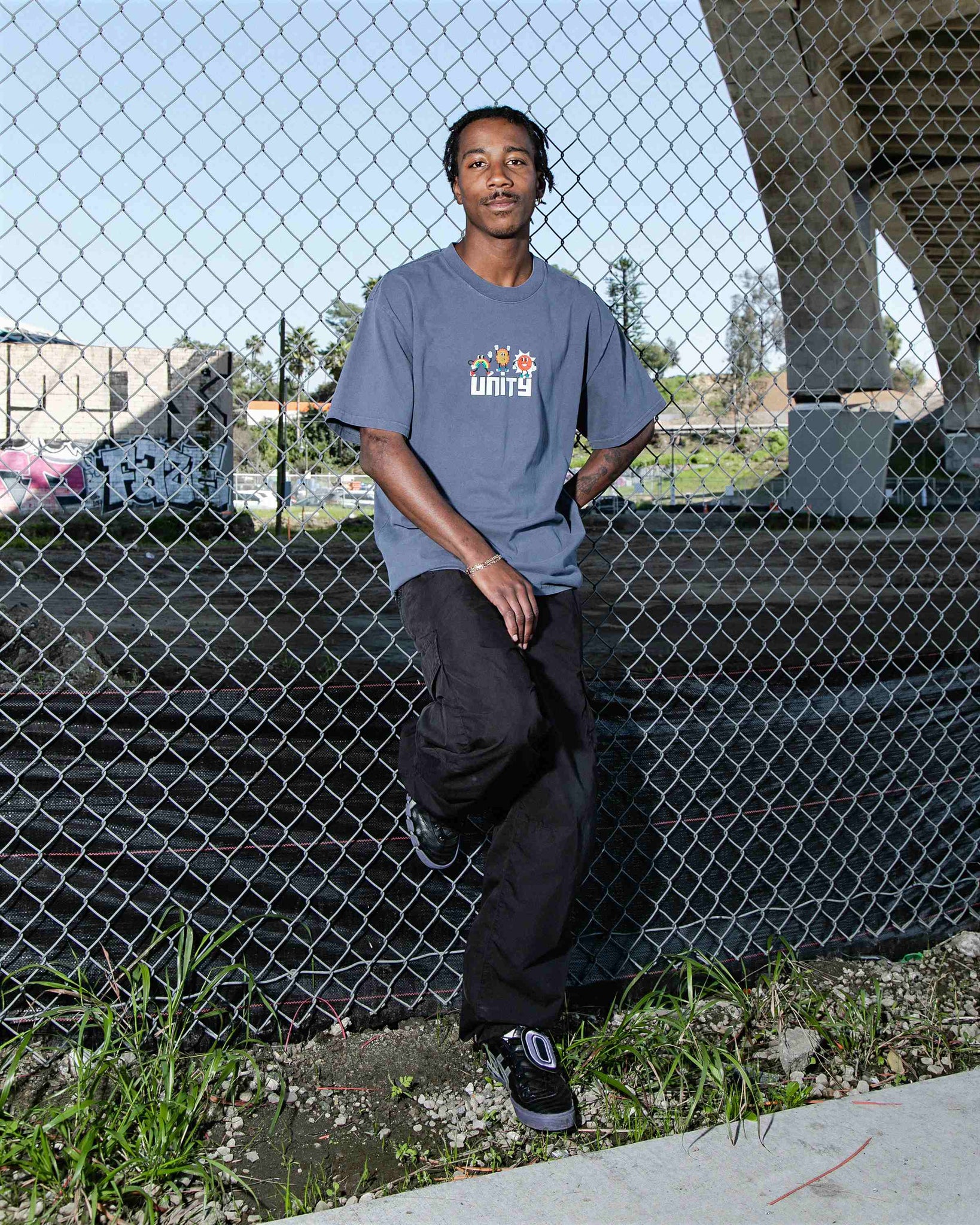 Close-up of male model leaning against fence wearing faded indigo oversized fit unisex cotton graphic t-shirt with Unity print