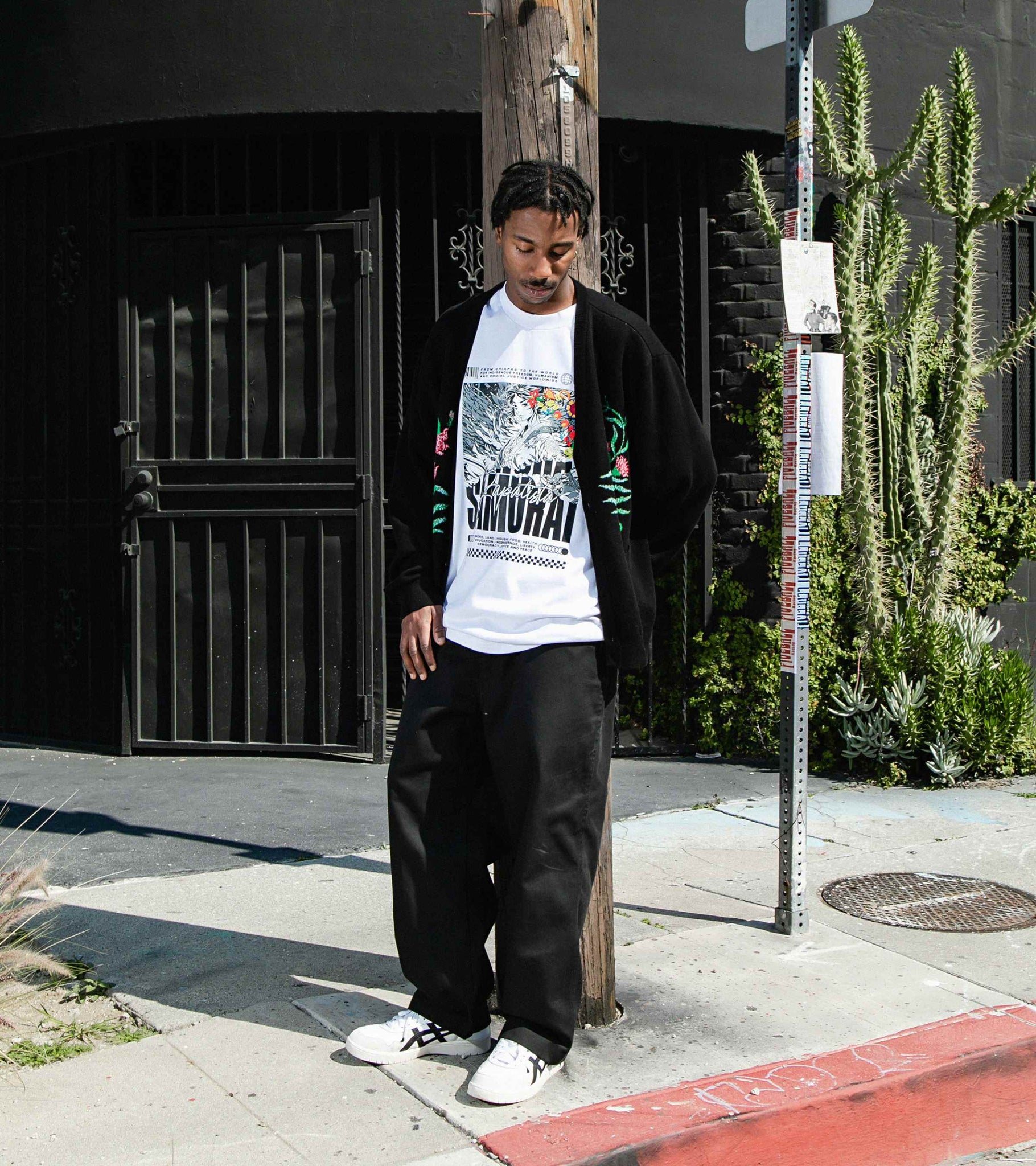 Wide shot of male model standing in the street and wearing white cotton graphic t-shirt with Zapatista Samurai print.